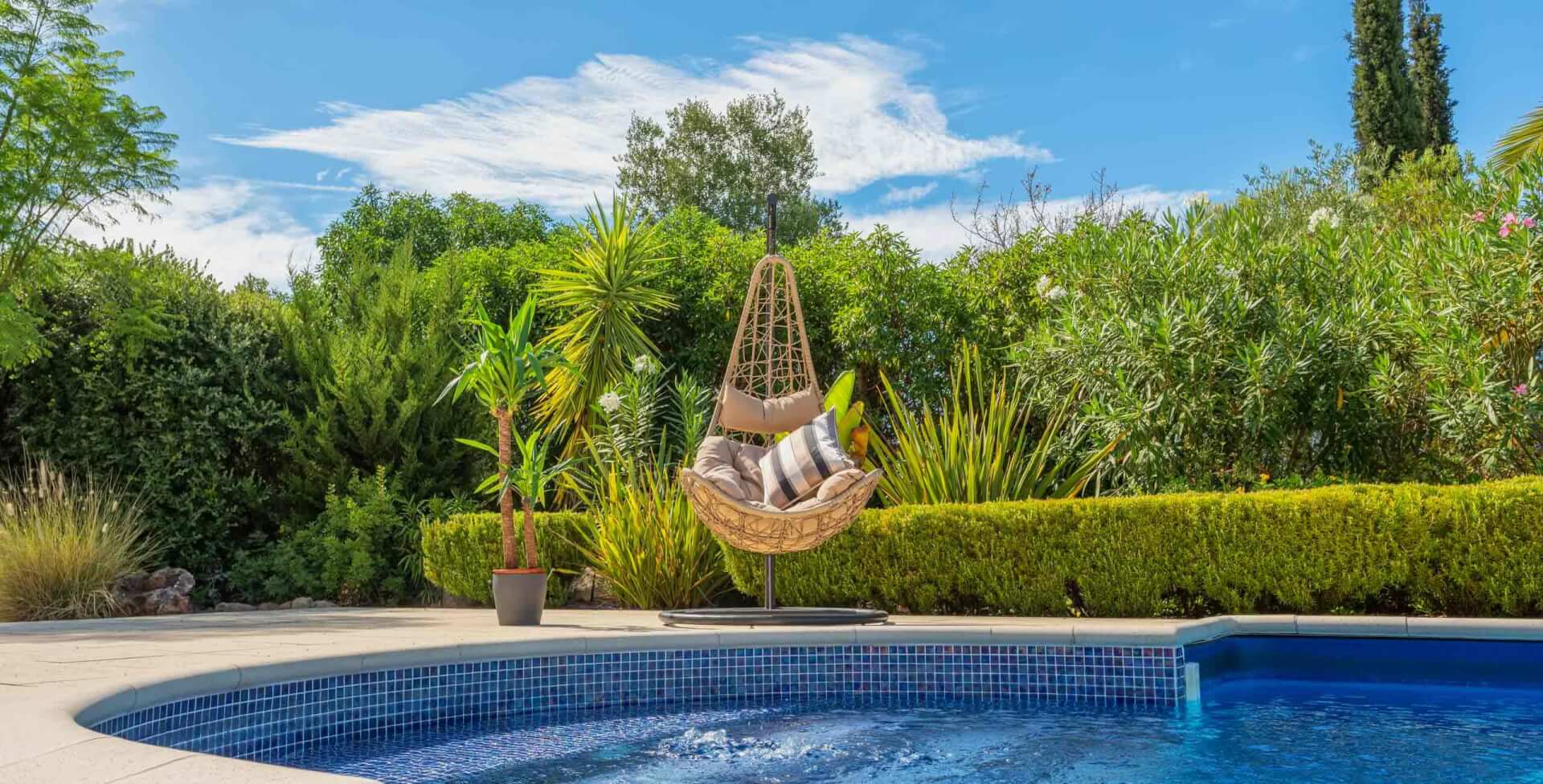 Luxurious pool in the garden of a private villa, hanging chair with pillows, in summer.