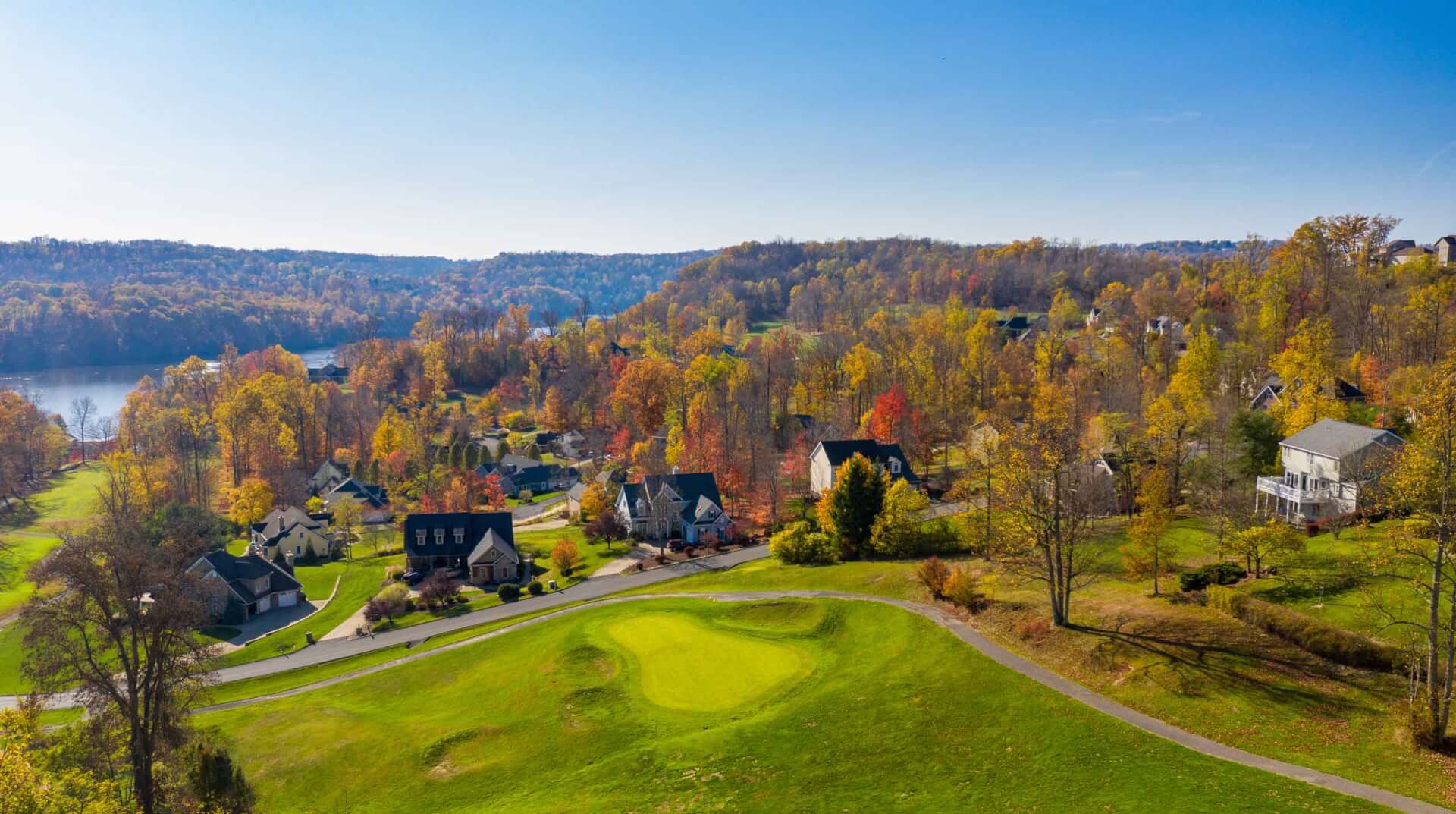 Aerial panorama of single family houses set among golf fairway and greens by a lake in autumn.